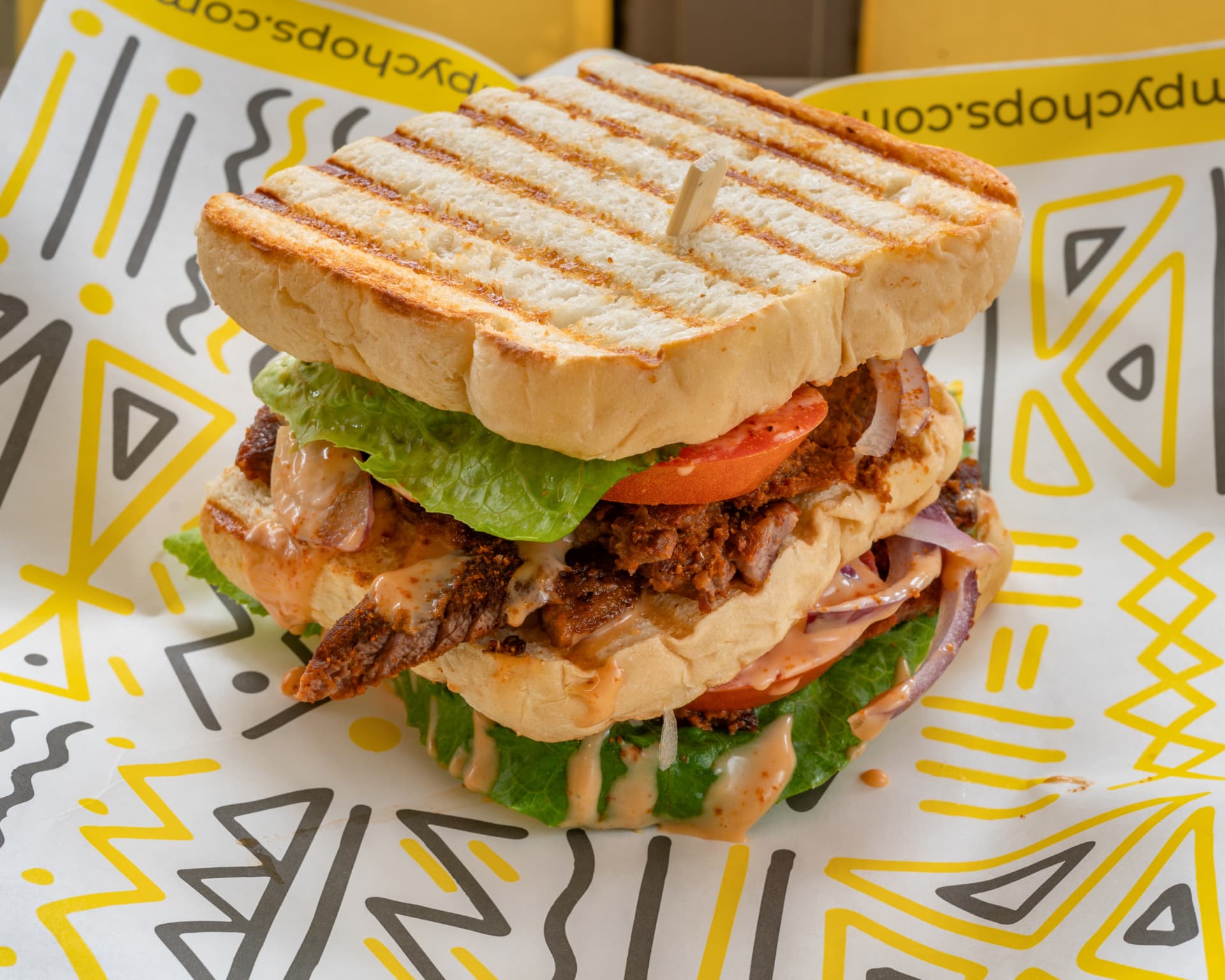 A SimplyChops grilled suya toast sandwich on branded wrapping paper
